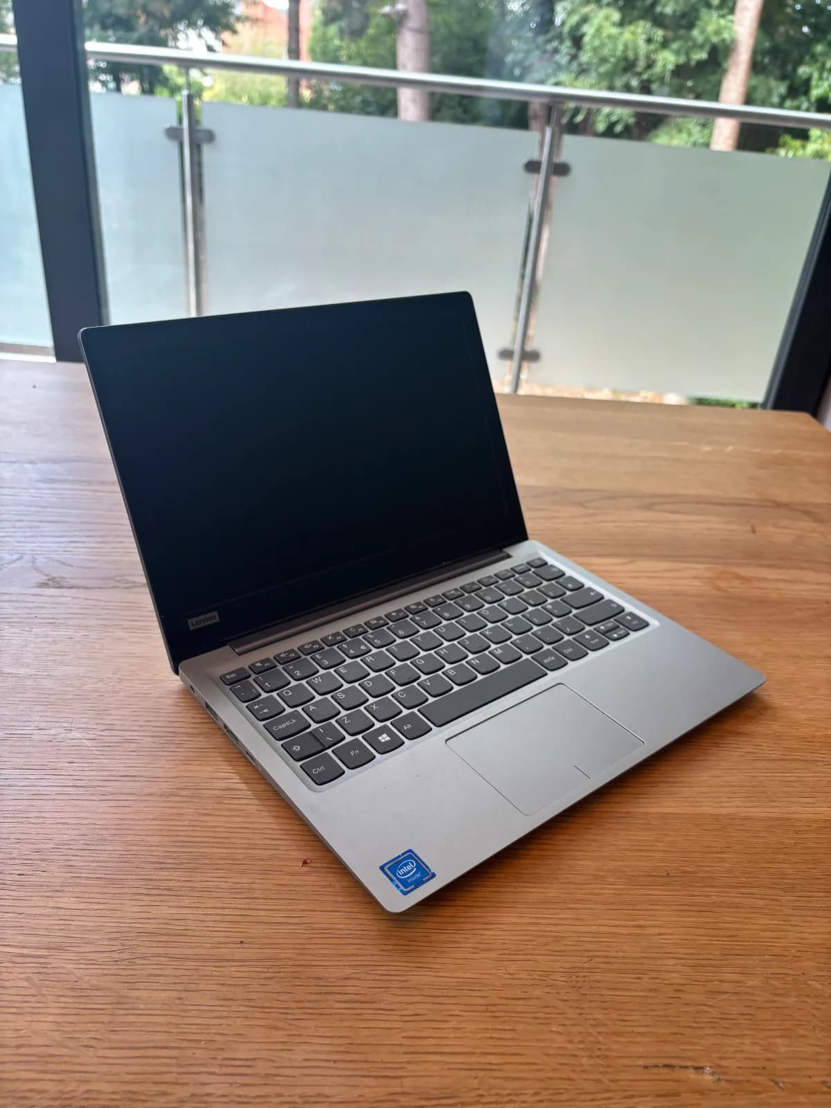This image shows the side view of the Lenovo. The Lenovo has black screen housing, a dark grey keyboard, a light grey base and a small touchpad in the centre.
